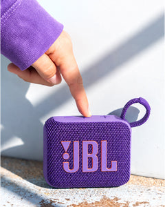 JBL Go 4 Taşınabilir Bluetooth Hoparlör Mor, bir elin kontrol tuşlarına bastığı dokulu ızgara detayı.